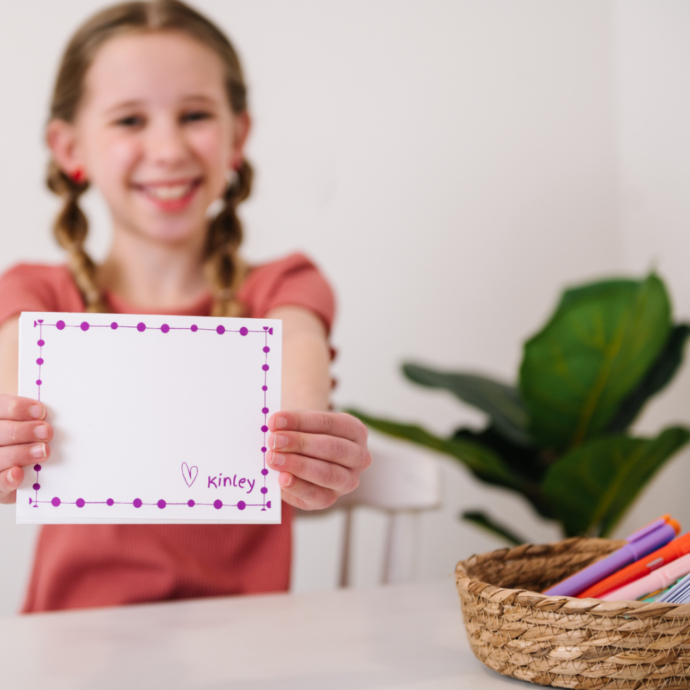 A girl smiles as she shows her new notecards that have been personalized with her name.