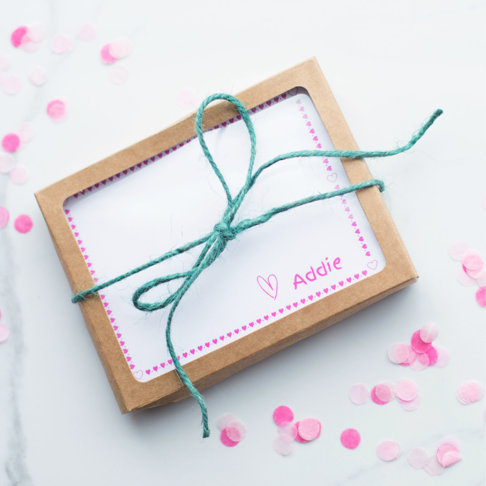 A set of personalized kids notecards in it's window box and kraft paper package, tied up with a bow.