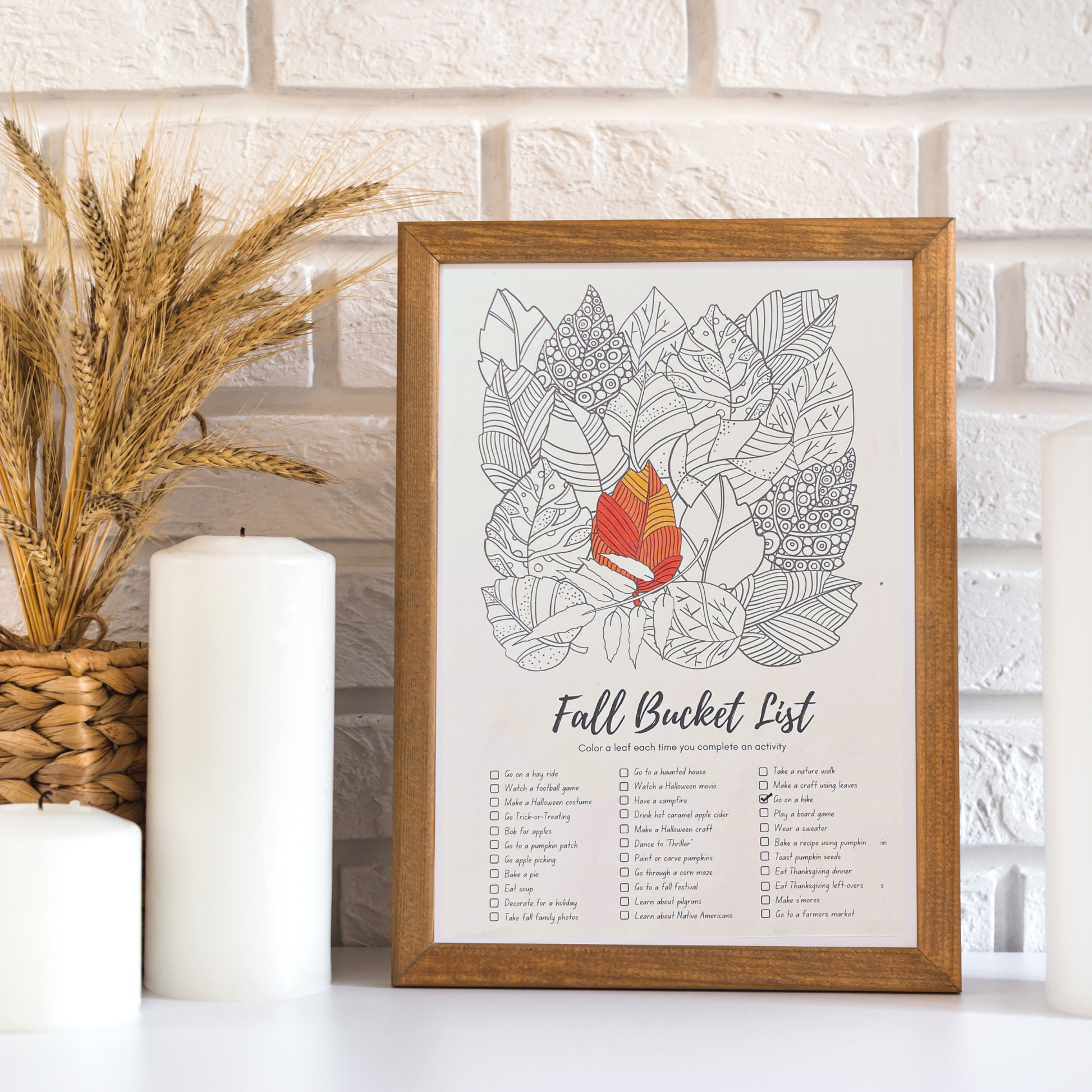 An example of the Fall Bucket List Coloring poster is framed and sitting on a counter with fall decor.