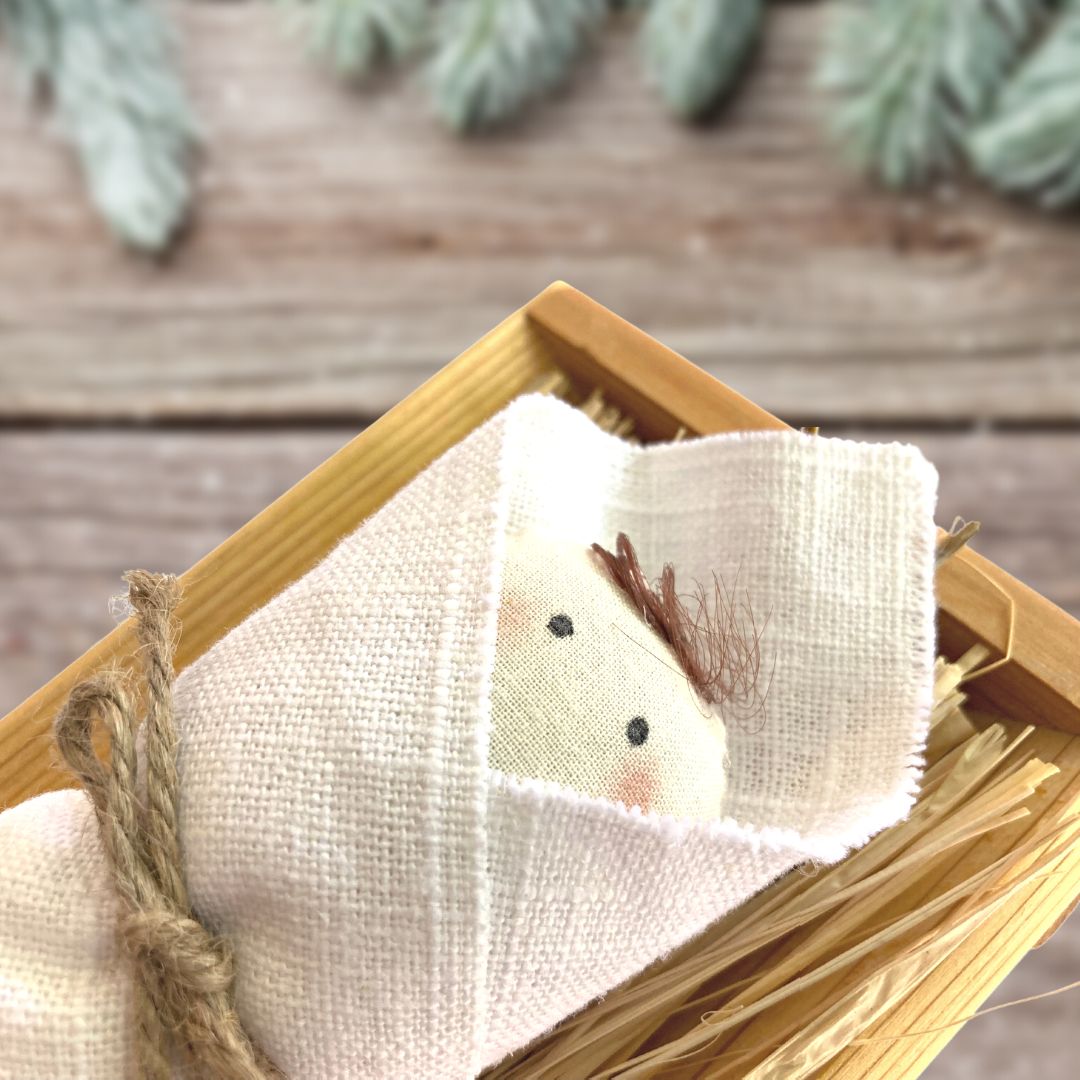 A cloth baby Jesus doll lays in a manger filled with hay.